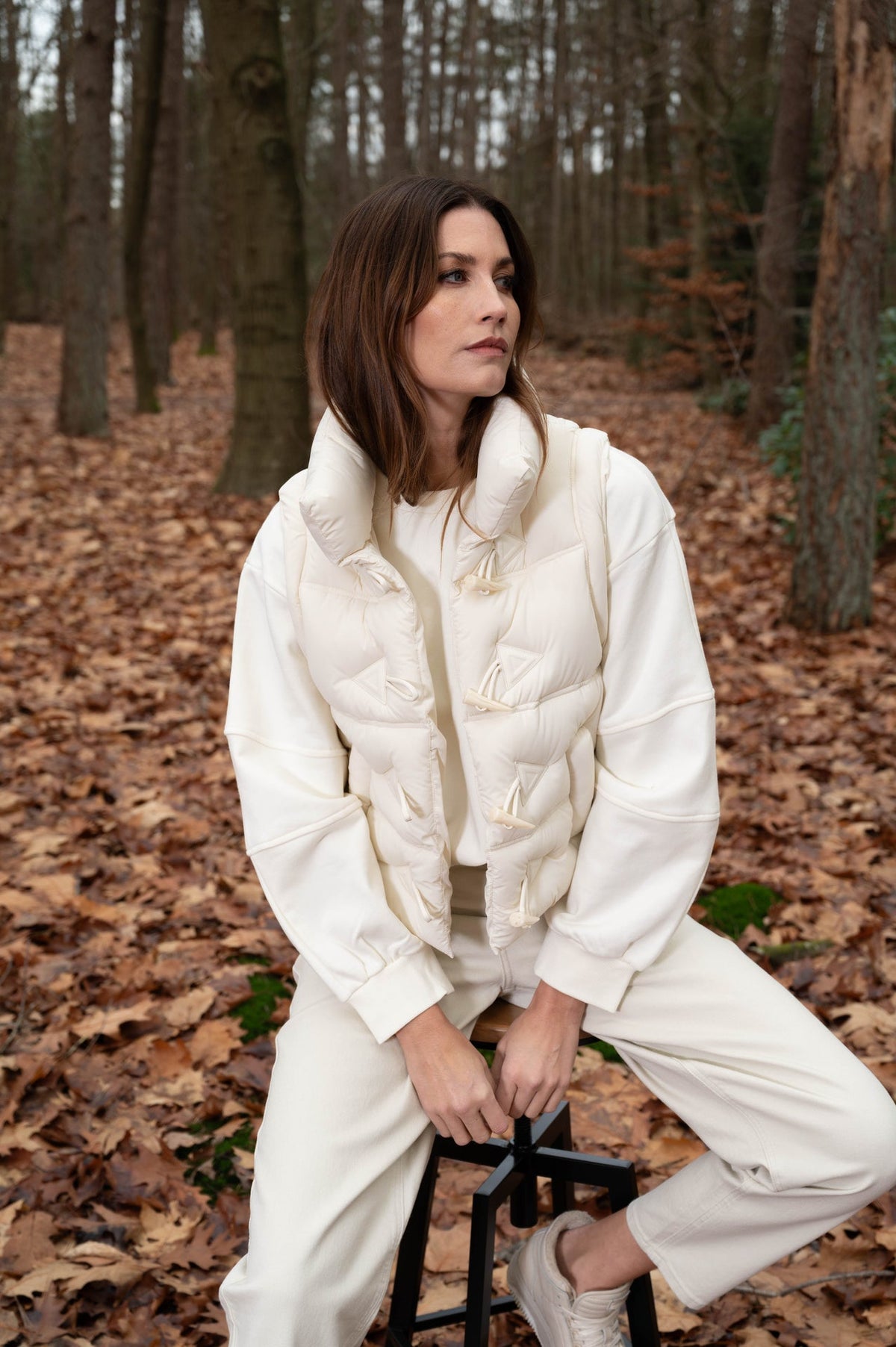 model met een complete off-white outfit met bodywarmer, trui en broek in dezelfde kleur