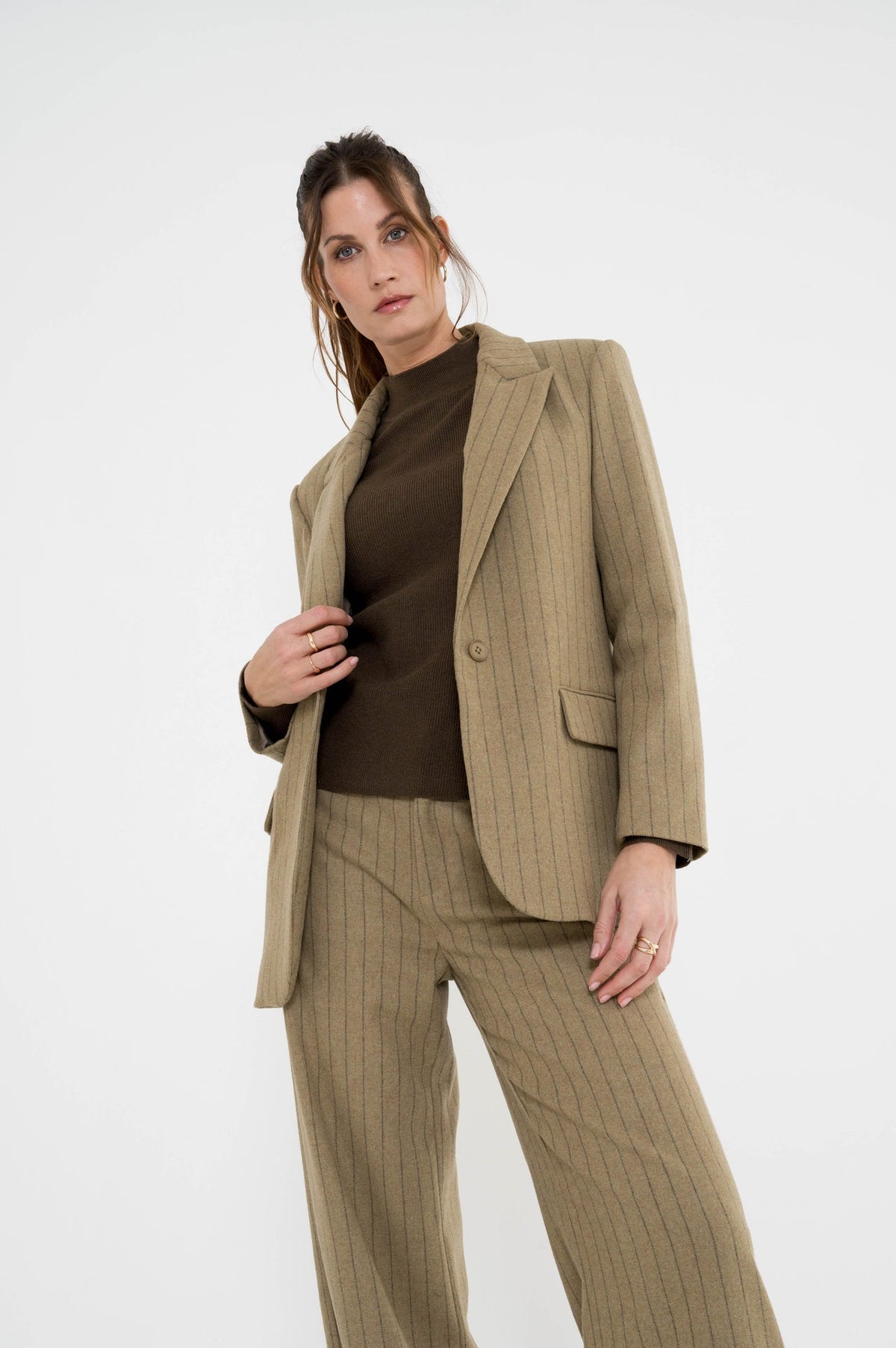 model draagt de mosgroene coltrui op een gestreepte broek met een gestreepte blazer in dezelfde kleur en stof
