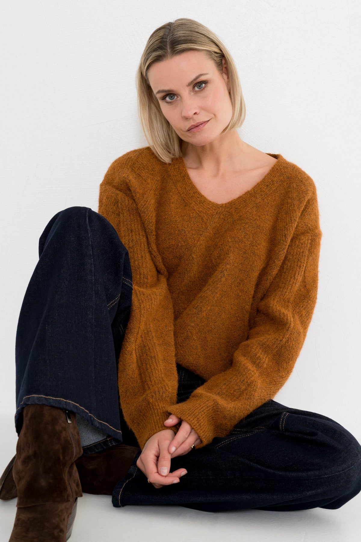 roestbruine dames trui met v-hals en ingebreid ruitmotief op een donkere spijkerbroek als herfstoutfit