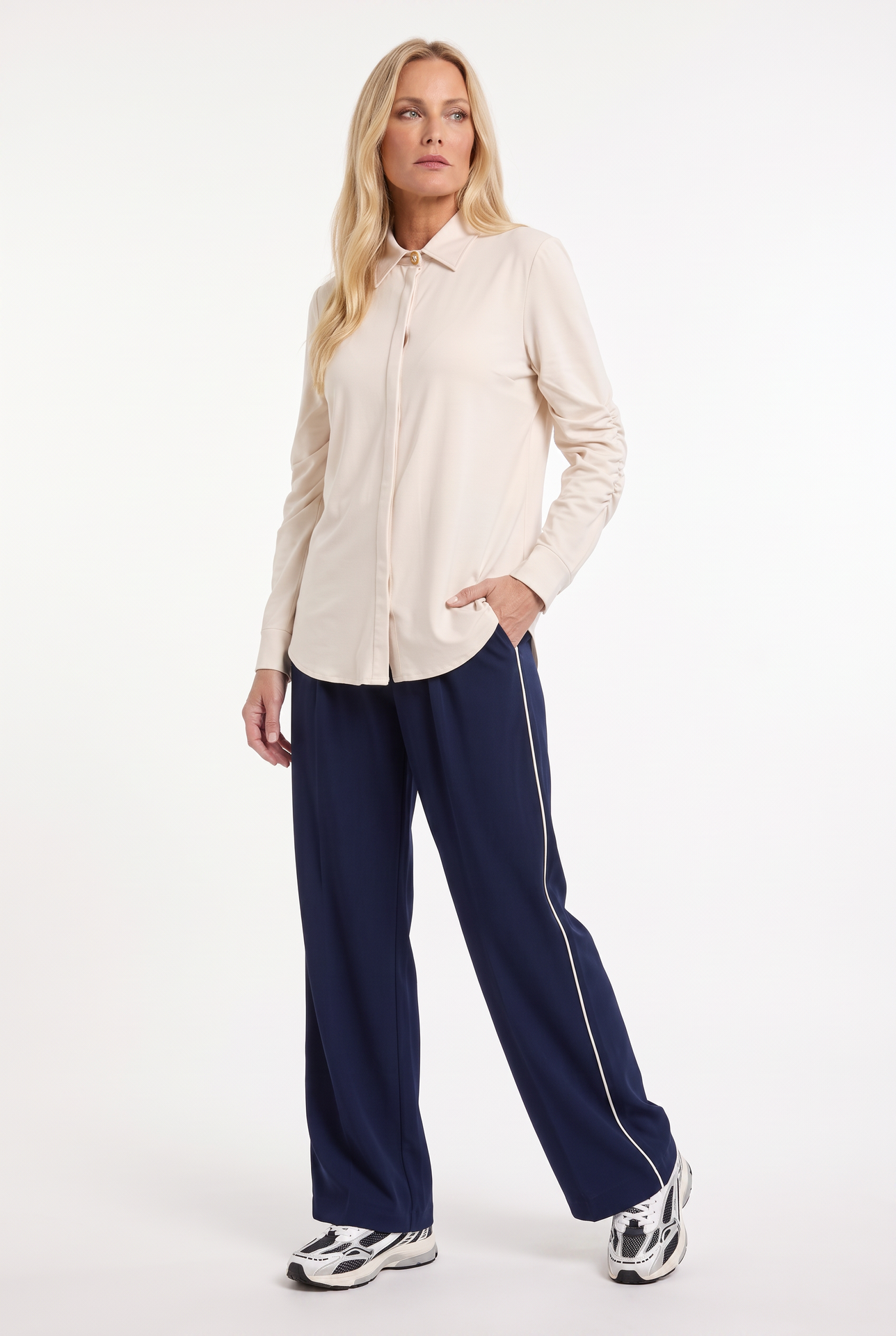model draagt sportieve outfit met donkerblauwe travelbroek met offwhite streep aan zijkant met daarboven een offwhite travelblouse