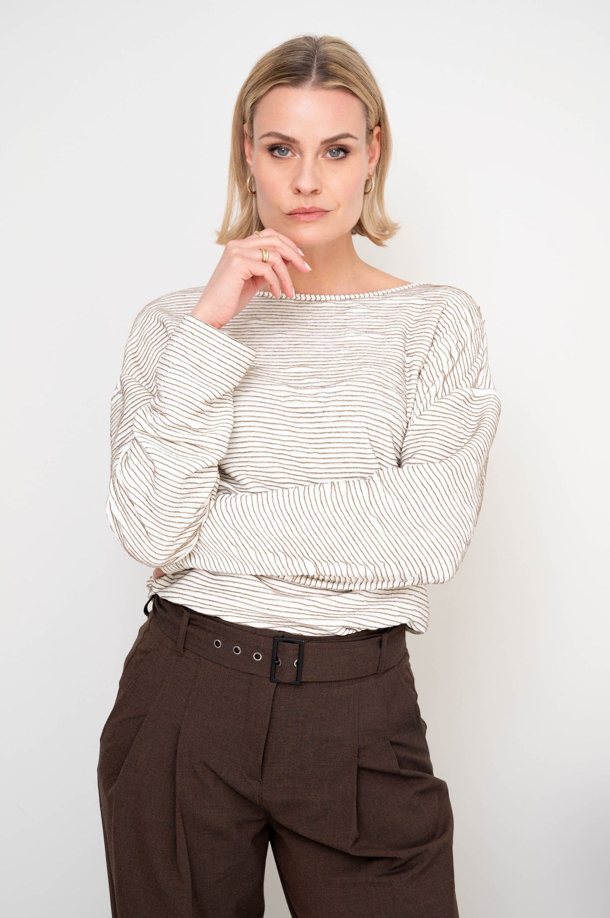 model draagt de zowy gestreept shirt van maicazz met losse fit en lange mouwen op een bruine broek
