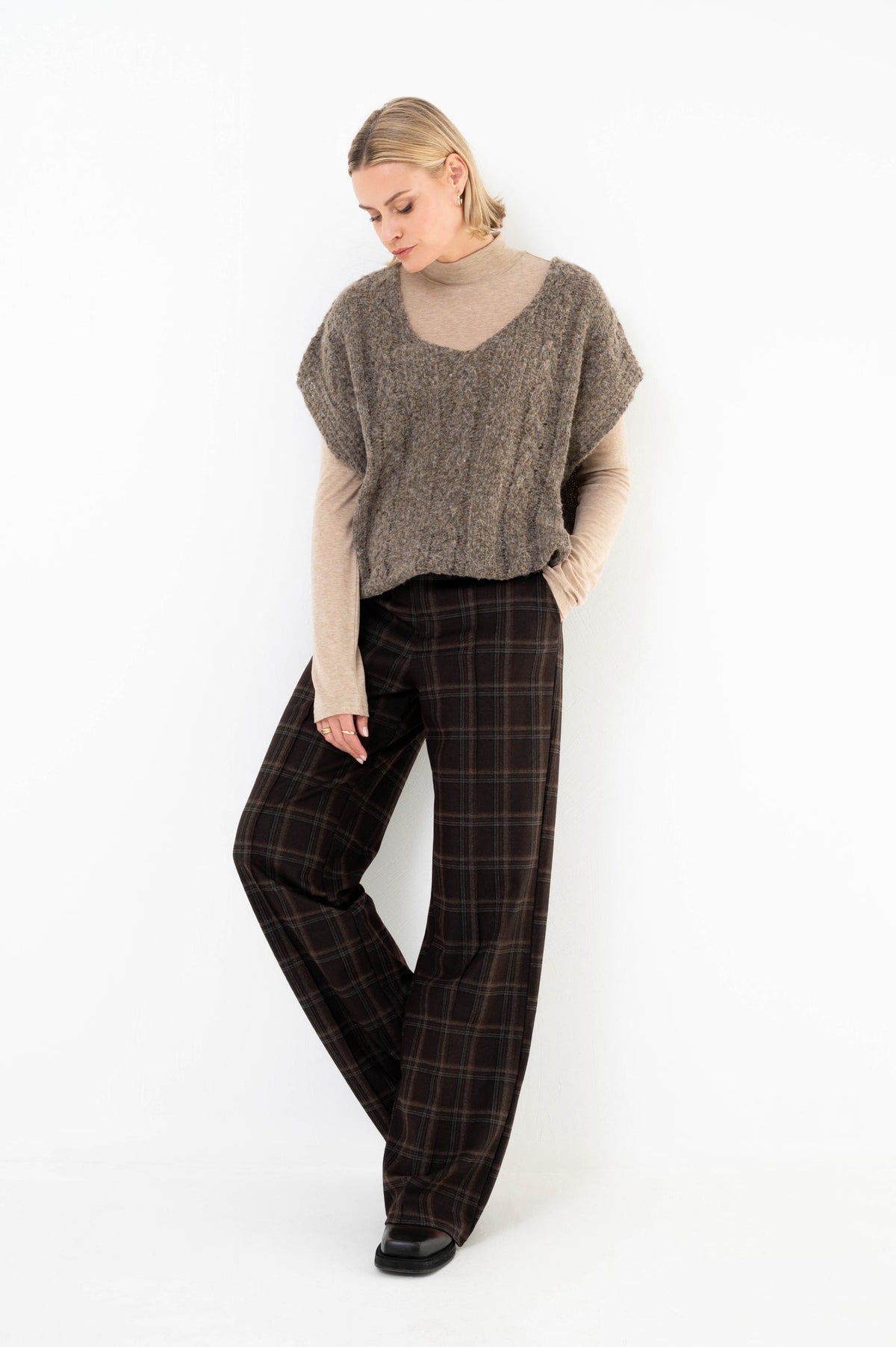 model draagt een bruin geruite broek in combinatie met een coltrui 