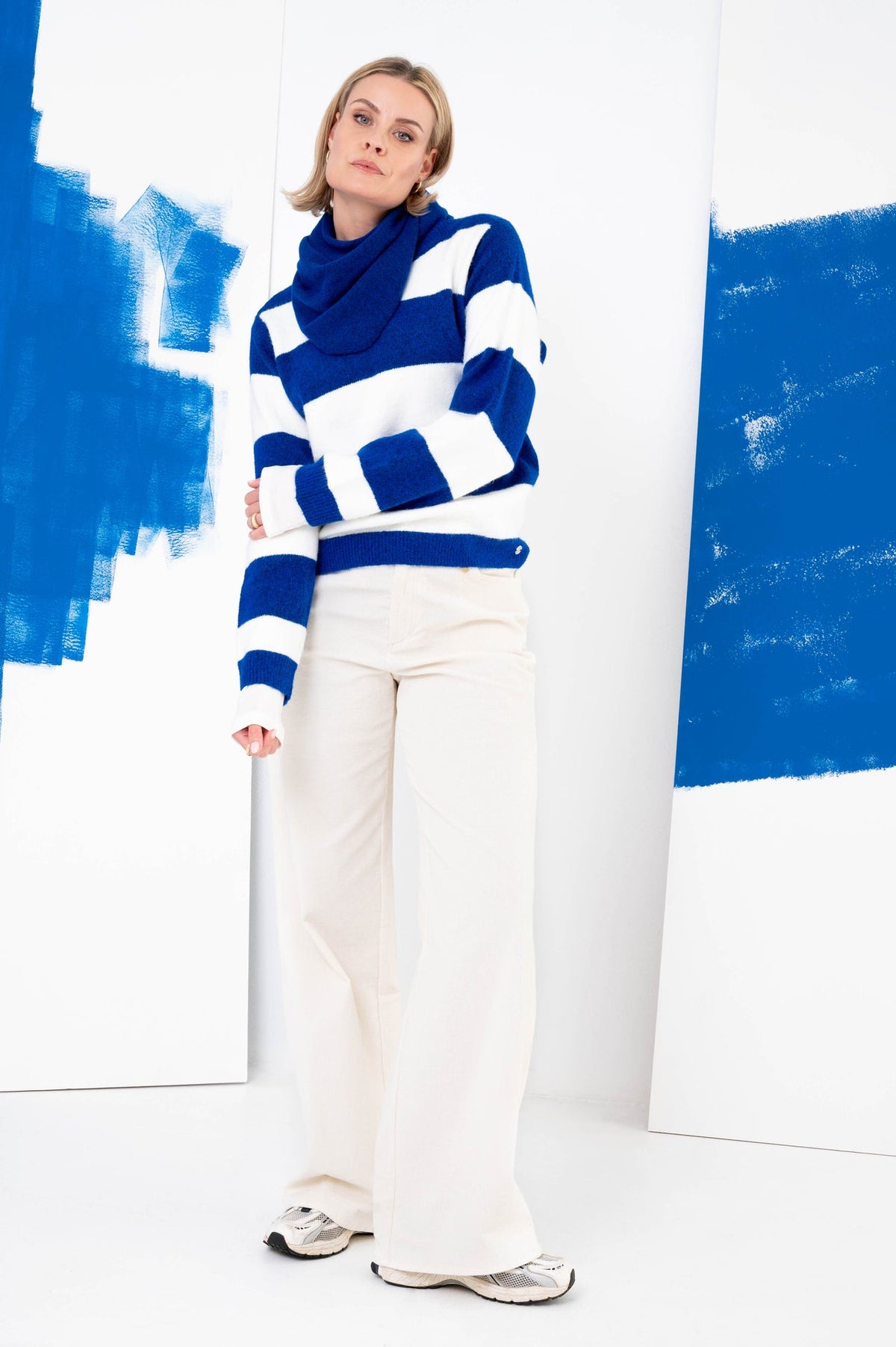 model draagt blauw-wit gestreepte trui met een bijpassende blauwe sjaal op een witte broek