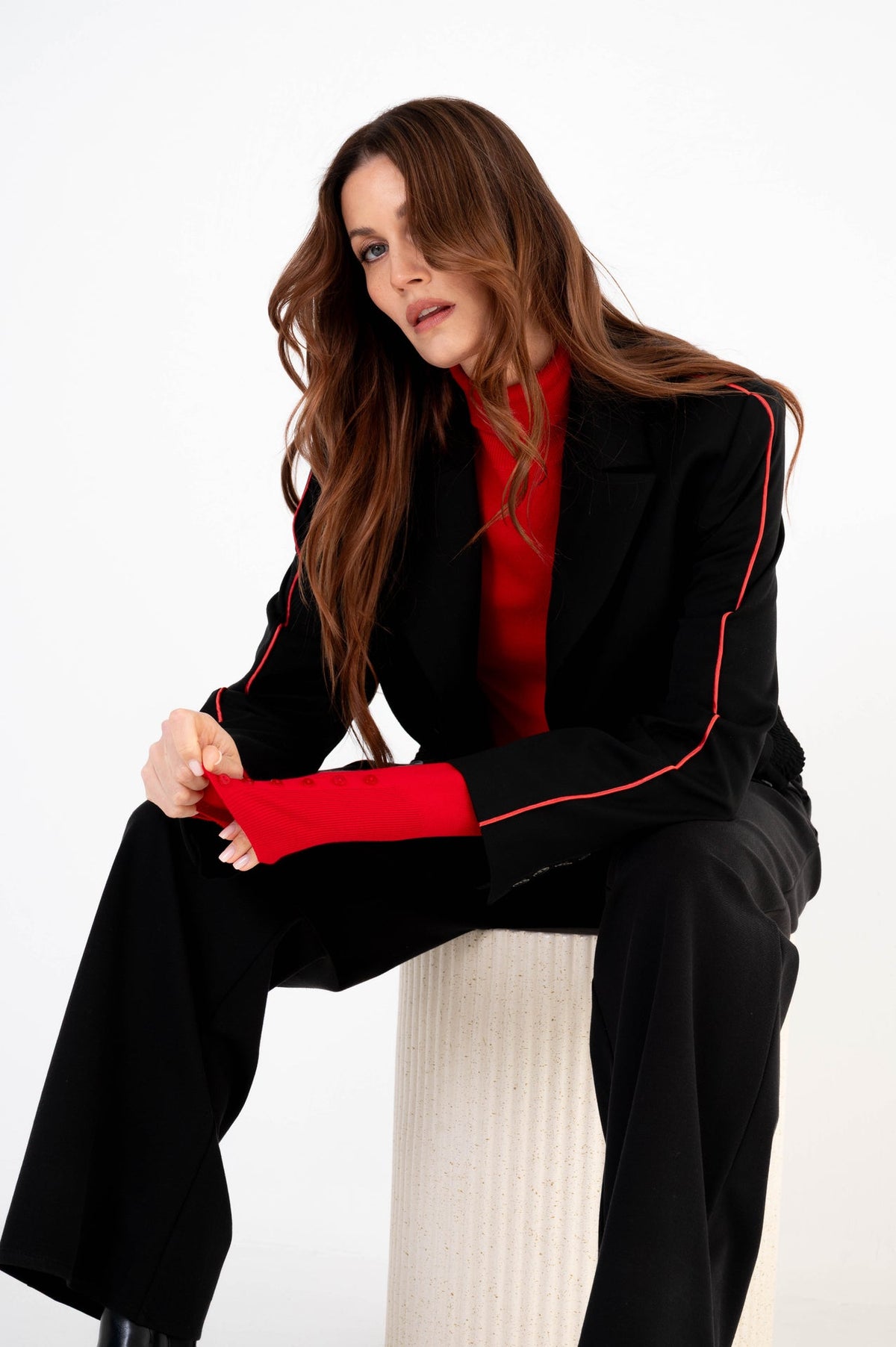 model draagt een blazer met rode streep aan de zijkant over een rode coltrui op een zwarte broek 
