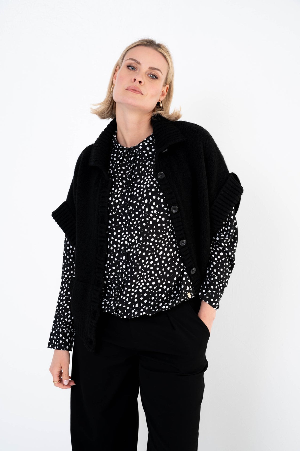 zwart gebreid vest met korte mouwen en knoopsluiting op een zwarte broek met zwart-witte blouse