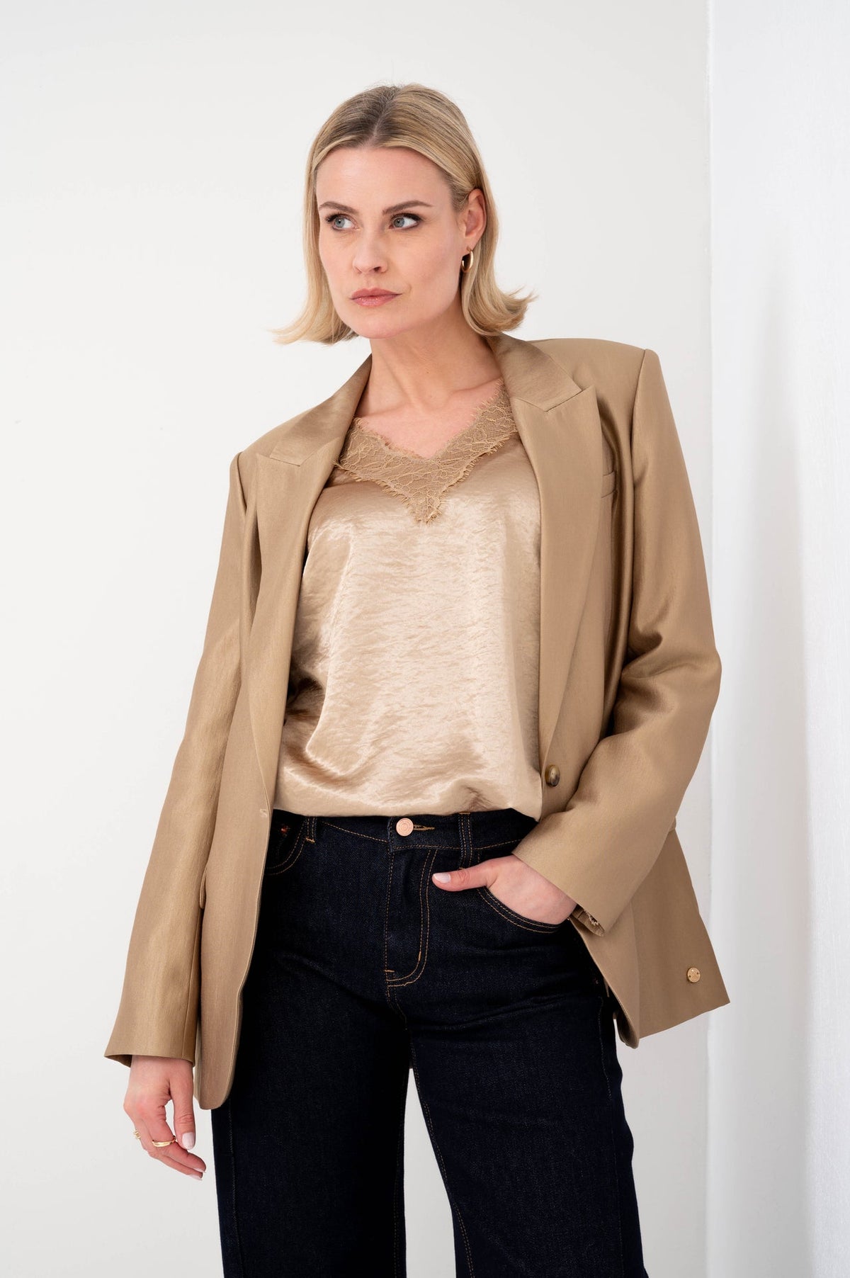 model combineert satijnlook shirt zoha van maicazz in goudkleur met gouden blazer zora van zizo op een donkere spijkerbroek